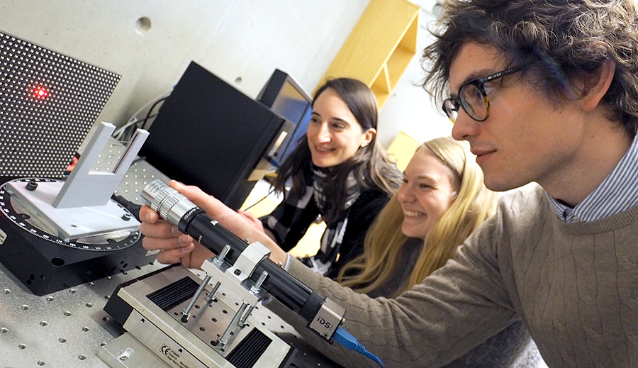 Three students in the physics lab doing an experiment with a red laser beam. Photo