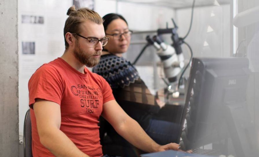 Two researches in a lab, with a microscope and a computer