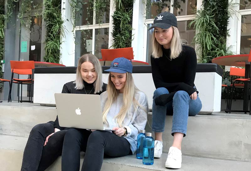 Three student sitting in a staircase lookling at a computer. Photo