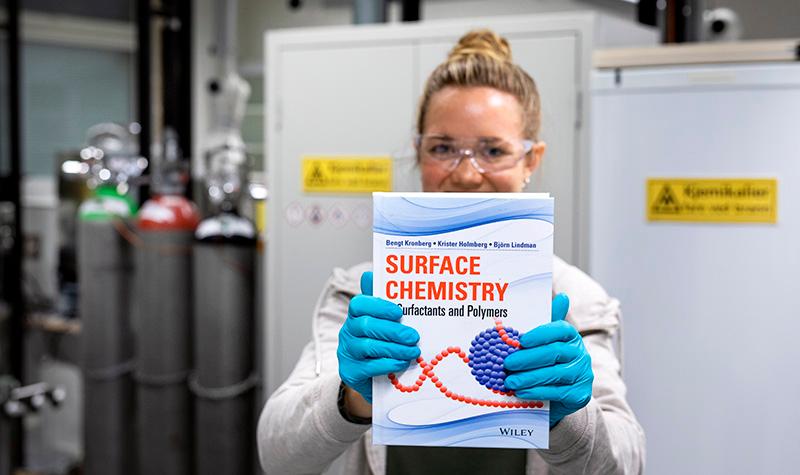 A student holding up the book Polymer Technology. Photo.