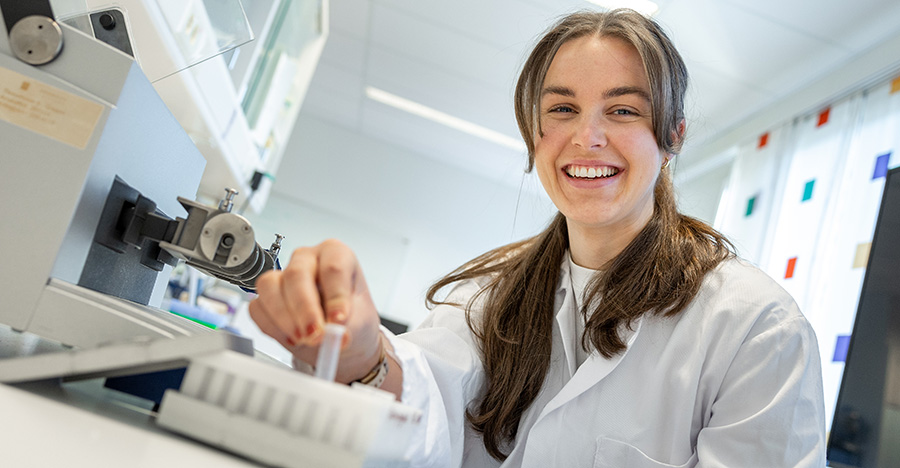 A student in a lab working and smiling