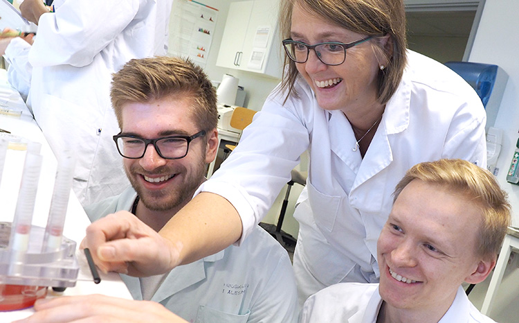 A professor showing two students an experiment in the lab