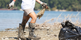 A person with boots picking plastic from a beach.