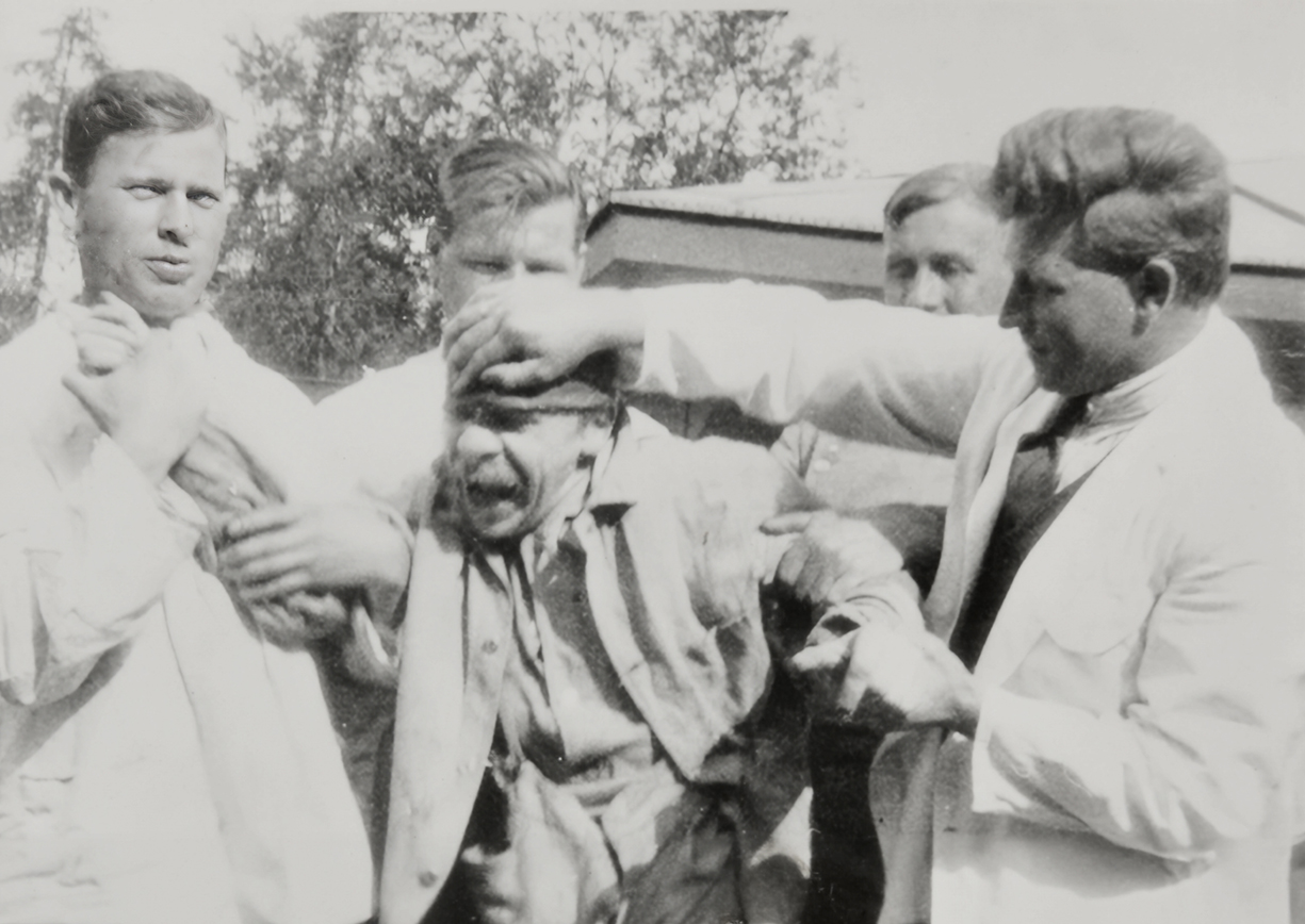 A patient being admitted to a mental asylum. He is physically restrained by three men wearing white coats