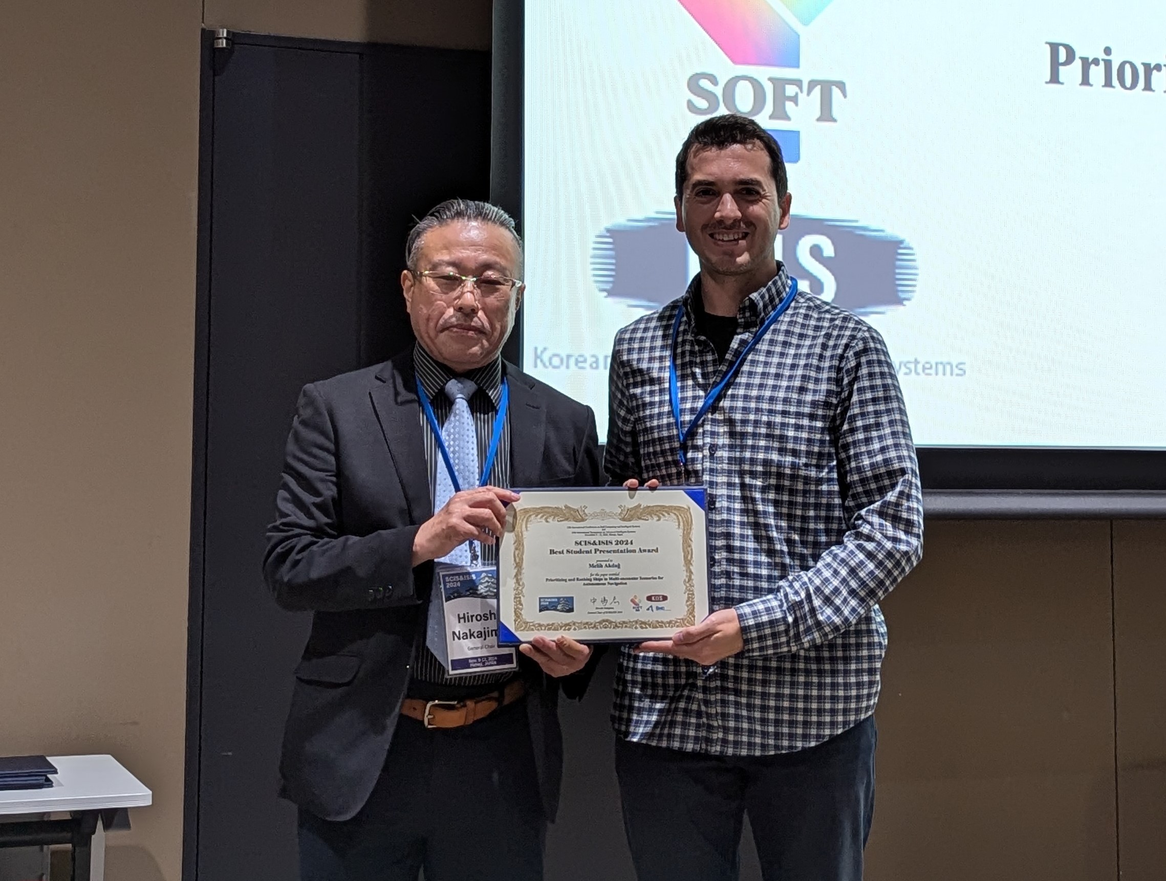 Melih Akdag on stage with the host of the session, accepting the diploma for Best Student Presentation.