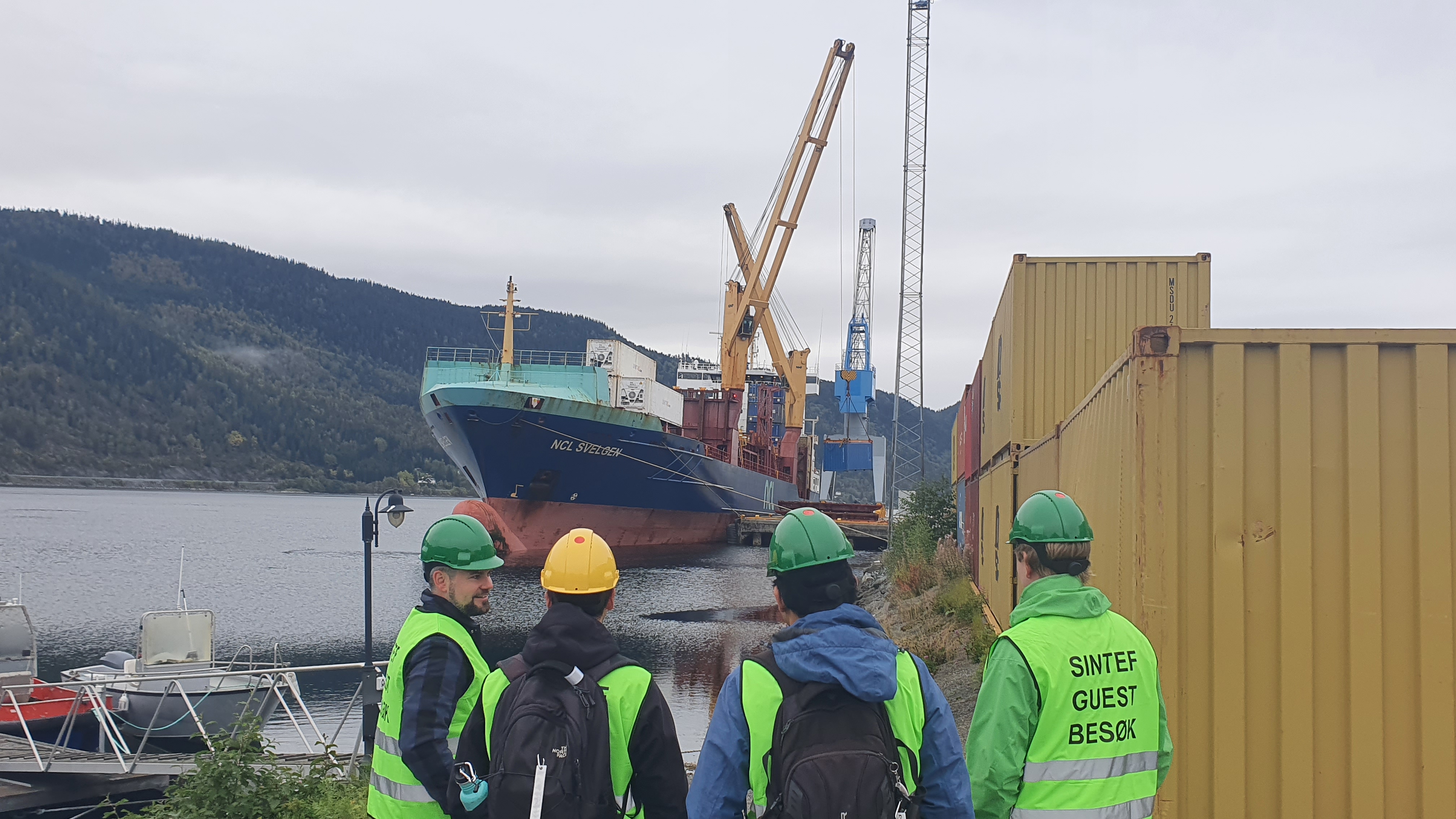 SFI AutoShip researchers seaside at Trondheim Havn container terminal in Orkanger, with the NCL vessel NCL Svelgen in the background.