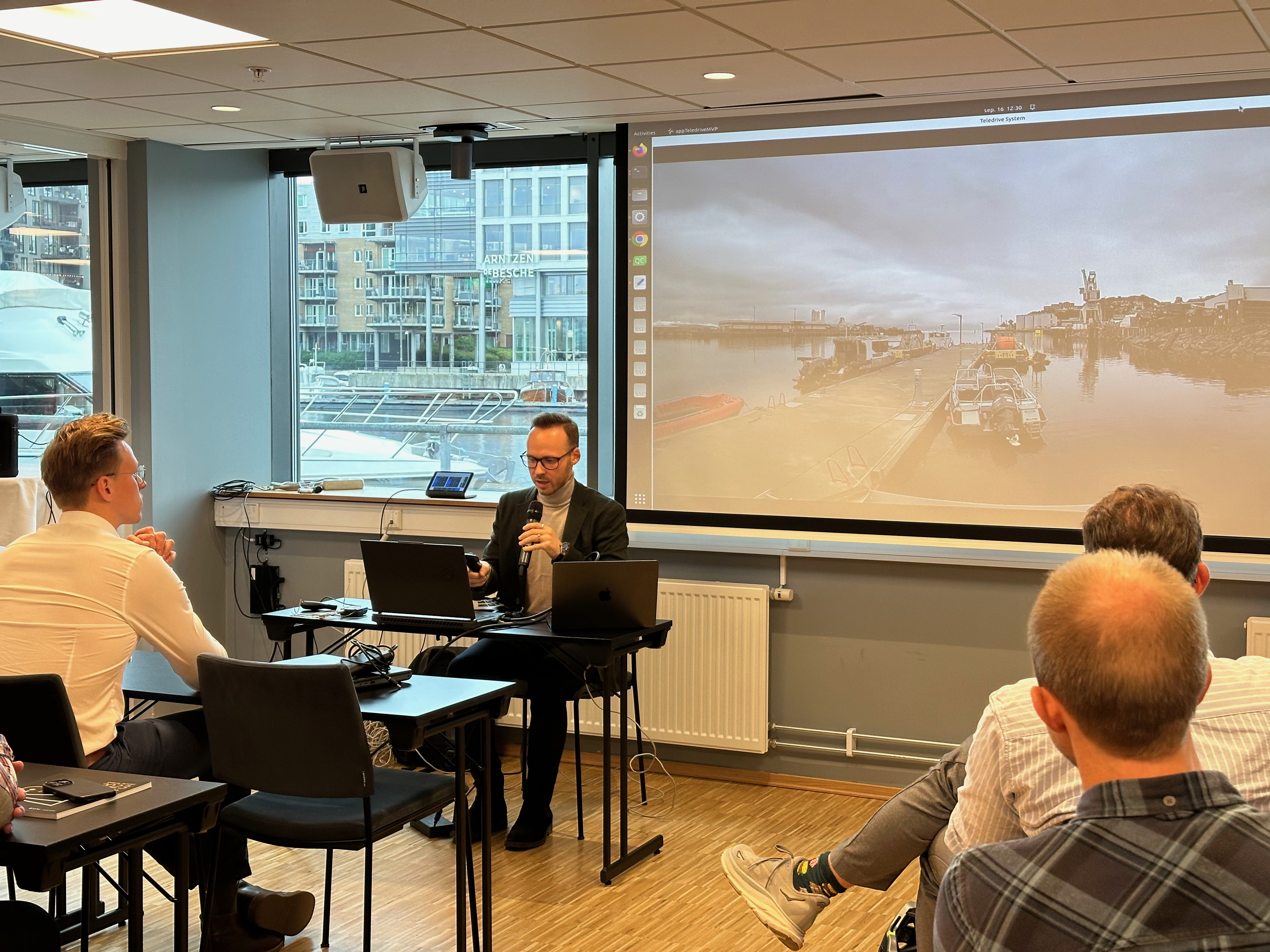 Alexey Gusev, researcher from the adjacent project Autoteaming, remotely controls the ferry milliAmpere 1 from the conference venue. The ferry is viewed by the audience by video link on the screen. 