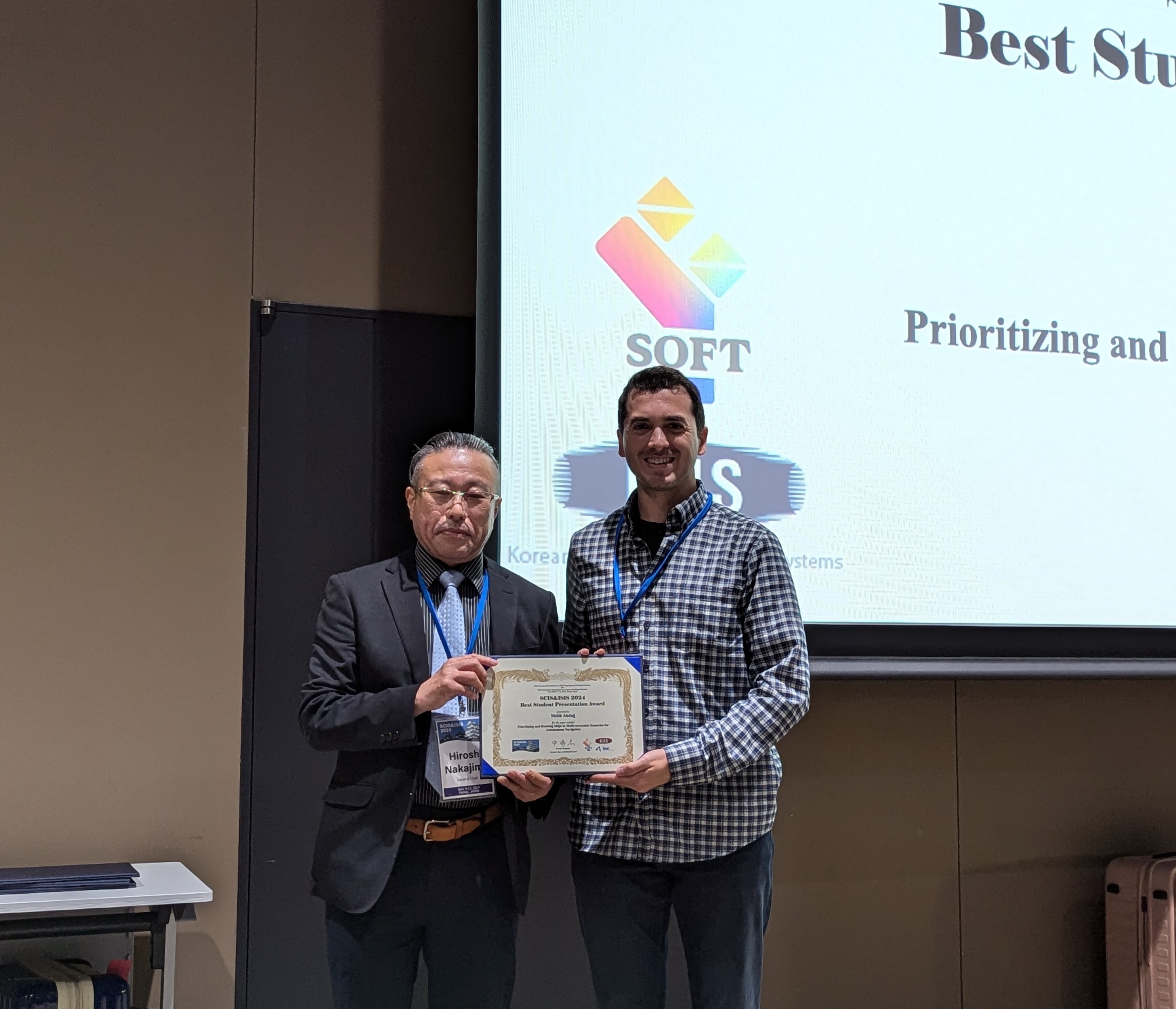 Host of session and Melih Akdag on stage with the award for the best student presentation.