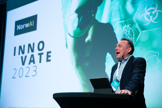 A person presenting at a podium with ‘NorwAI INNOVATE 2023’ on the screen.