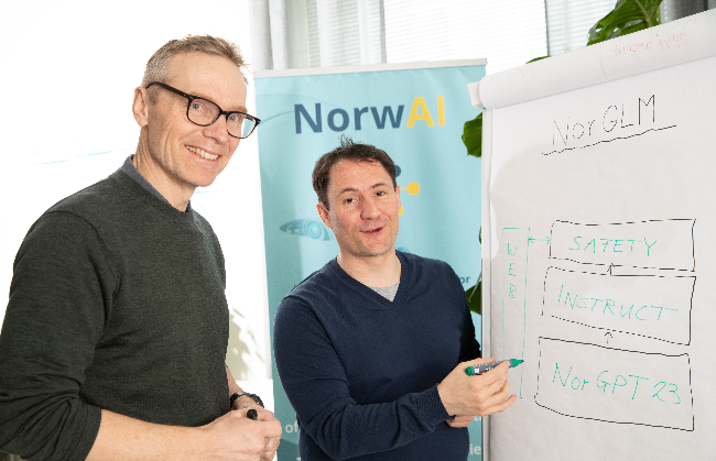 Two individuals discussing notes on a whiteboard next to a NorwAI banner