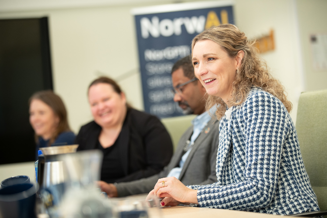 Four people sitting at a table during a meeting with a ‘NorwAI’ poster in the background