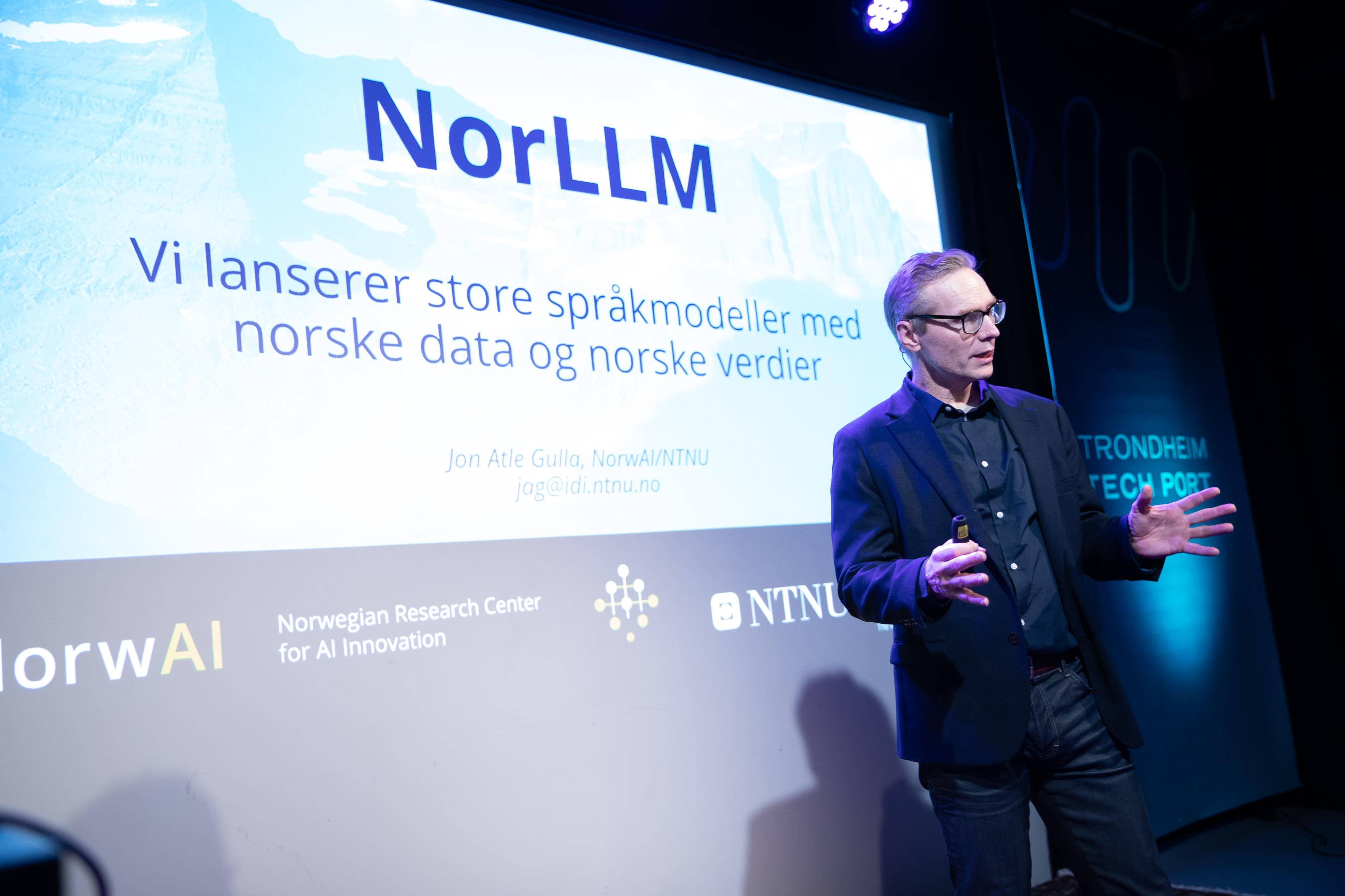 A presentation of the NorLLM project, which focuses on large language models based on Norwegian data and values, at a conference in Trondheim. The screen displays information about the model launch, along with the logos of NorwAI and NTNU