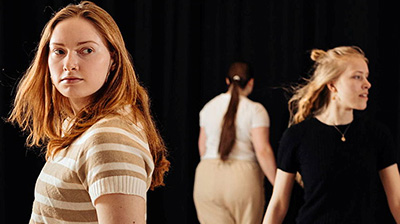 A photo of a student theater production where three young female studentswalk in different directions.