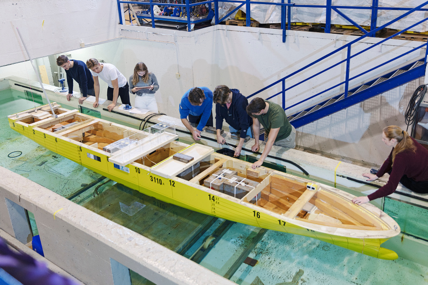 A group of students is standing around a pool looking at a model boat.