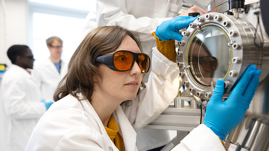 A researcher looking into research equipment with two researchers in the background