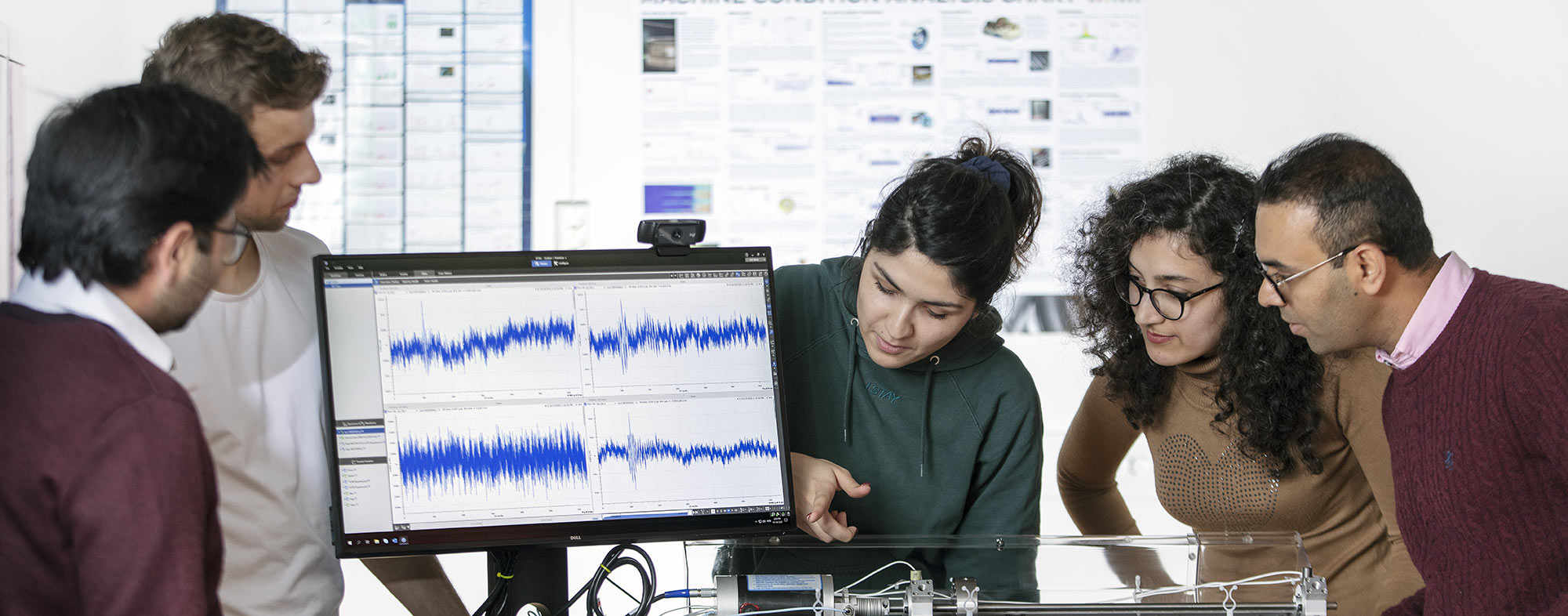 A group of individuals analyzing waveforms on a computer monitor in a laboratory setting.