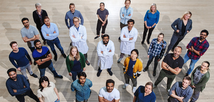 A research group stands on the floor in a fan shape, looking up at the photographer.